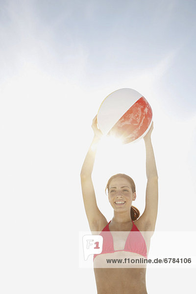 Young woman holding beach ball above head