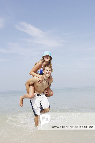 Young man carrying girlfriend on back in ocean
