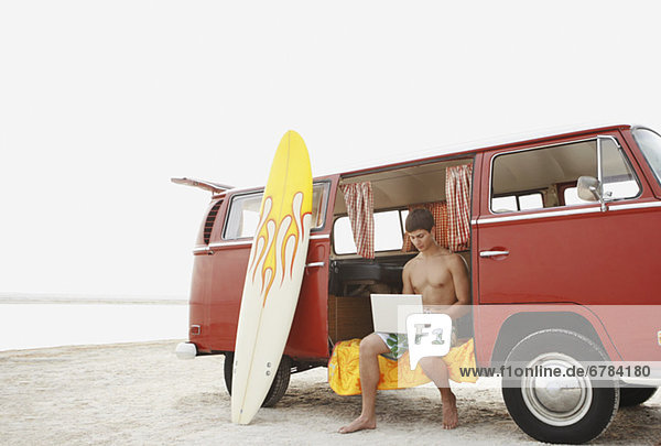 Young surfer using laptop in van on beach