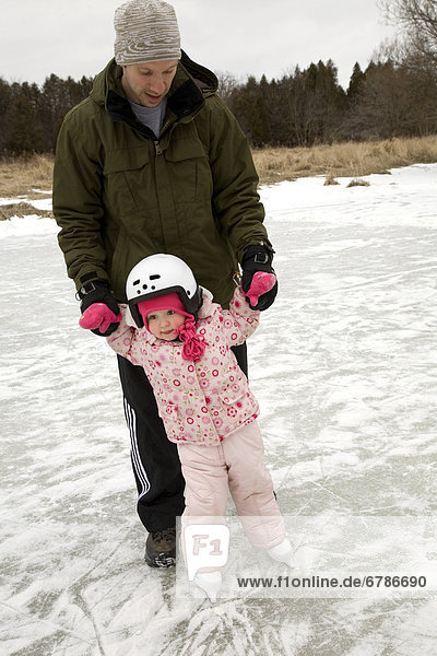 Dad teaching daughter to skate on an outdoor pond  Ontario