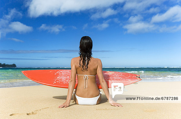 Hawaii  Kauai  Woman sitting on beach with surfboard  View from behind.