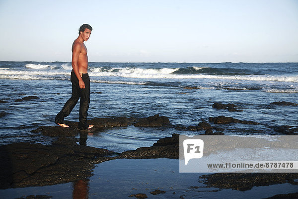 Hawaii  Oahu  Attractive male walking along the black shoreline rocks.