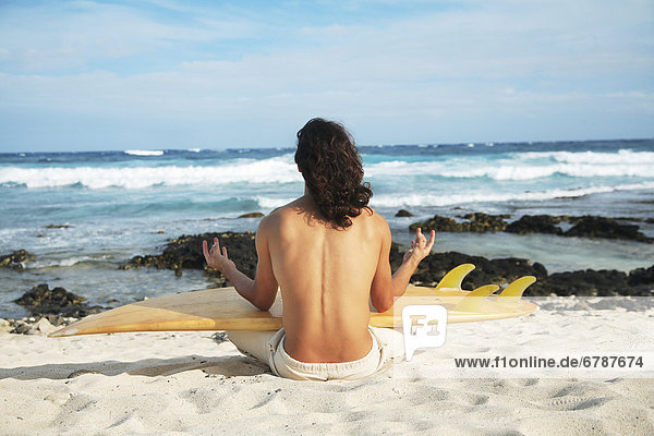 Hawaii  Oahu  junger Mann am Strand Meditieren mit Surfboard.