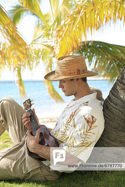 Hawaii  Oahu  Young male mit Vintage hat aloha Shirt und Stroh entspannenden halten einer Ukulele.