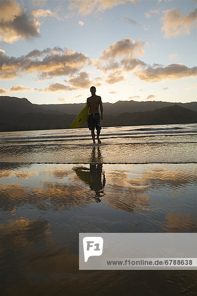 Hawaii  Kauai  Hanalei Bay  junger Mann am Strand zu Fuß mit Surfboard bei Sonnenuntergang.