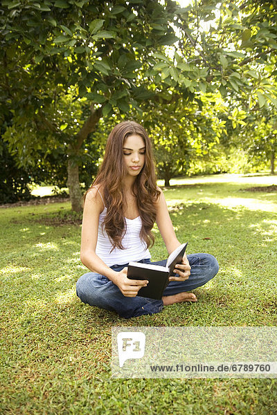 Hawaii  Kauai  Attractive young woman in the park reading a book.