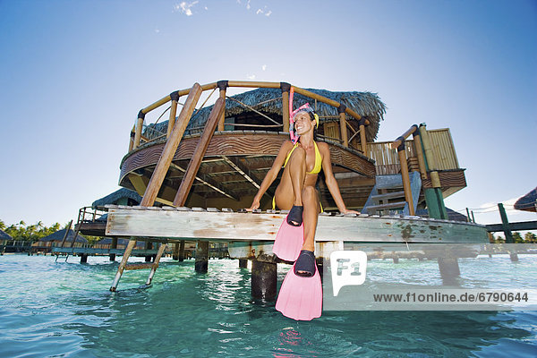 Französisch-Polynesien  Bora Bora  Frau sitzt auf dem Dock eines Bungalows vor Schnorcheln.