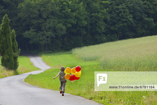 Junge  6 Jahre  läuft mit bunten Luftballons Weg entlang