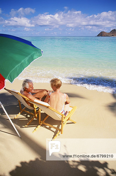 Senior couple sitting in chairs under umbrella on the beach  turquoise ocean