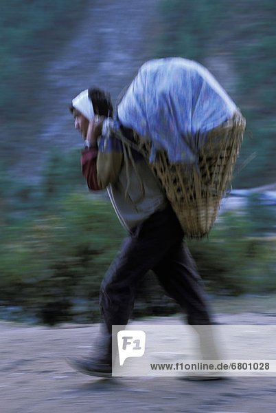 Man Carrying Heavy Basket Along Path