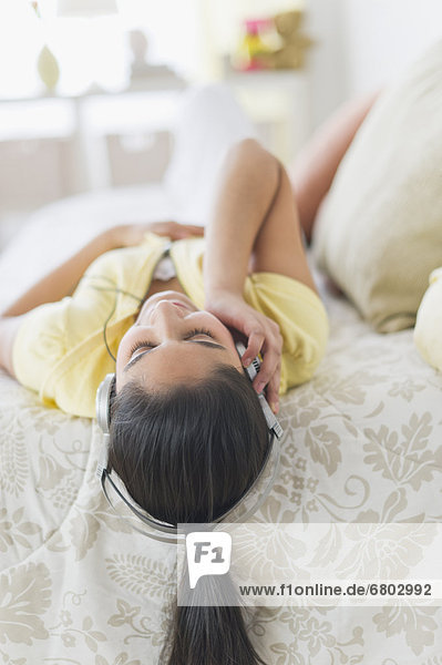 Girl (12-13) lying on bed with headphones