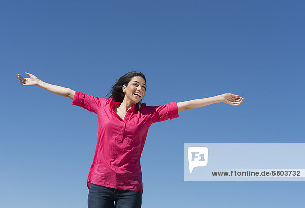 Young woman outstretching arms against blue sky
