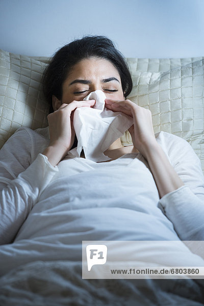 Young woman blowing nose in bed