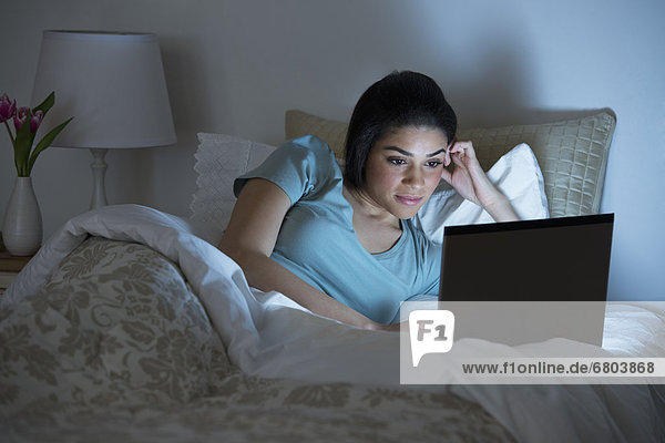 Junge Frau mit Laptop im Bett