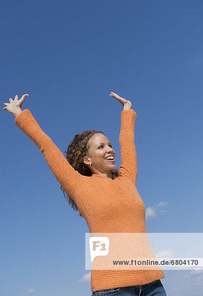 Mature woman with arms raised towards blue sky