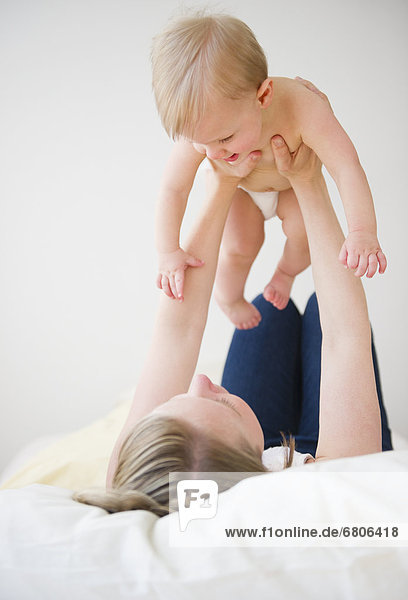 Mother lying on bed and lifting son (6-11 moths)