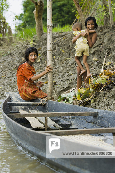 Three Girls With A Boat At The Water's Edge Of Surma River In A Rural Area Near Sylhet  Bangladesh