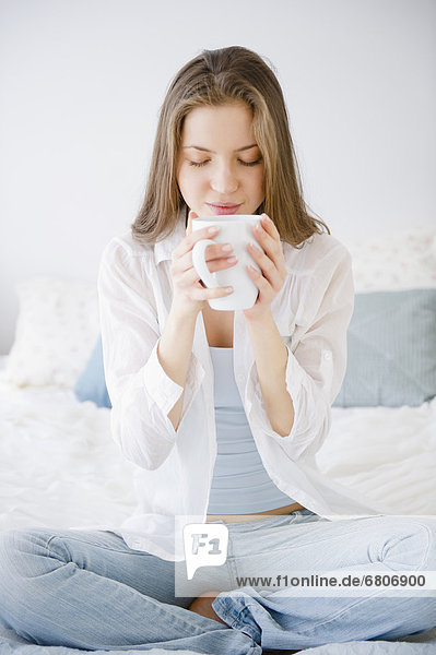 Woman sitting on bed drinking coffee