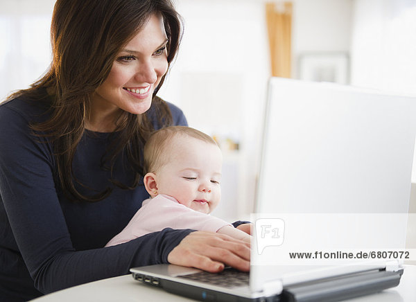 Mother with baby daughter (6-11 months) using laptop