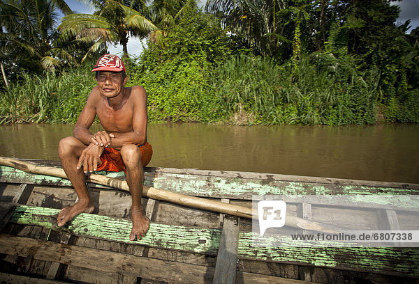 A Shirtless Man Sits In A Wooden Boat Along The Water  Tanjung Lubuk Sumatera Selatan Indonesia