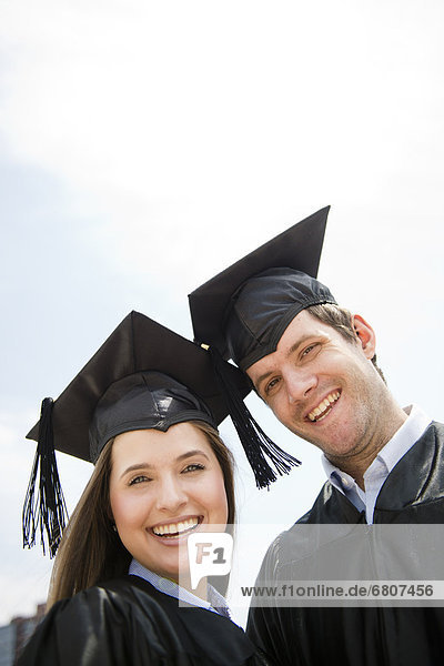 Young man and woman wearing graduation gowns