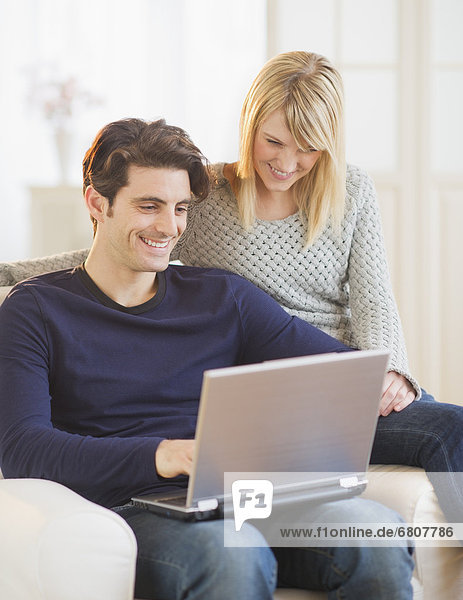 Couple sitting together on armchair and using laptop