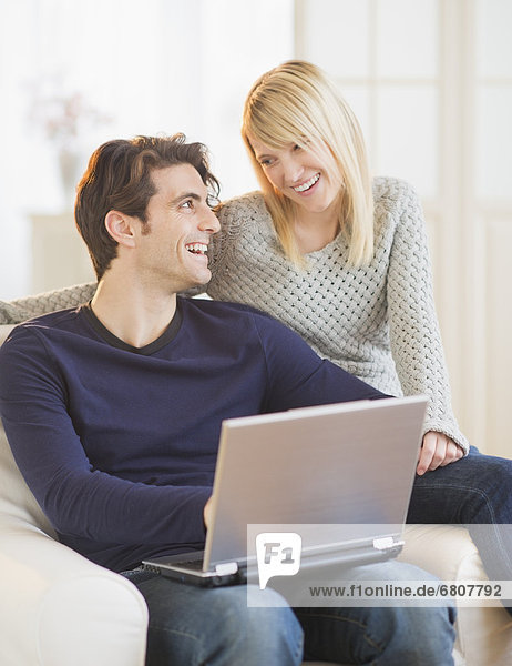 Happy couple sitting together on armchair and using laptop