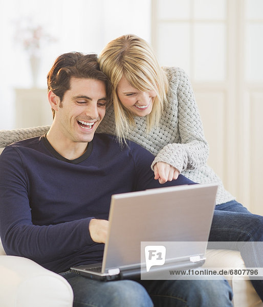 Happy couple sitting together on armchair and using laptop