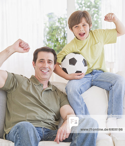 Father and son (10-11 years) watching football match with excitement