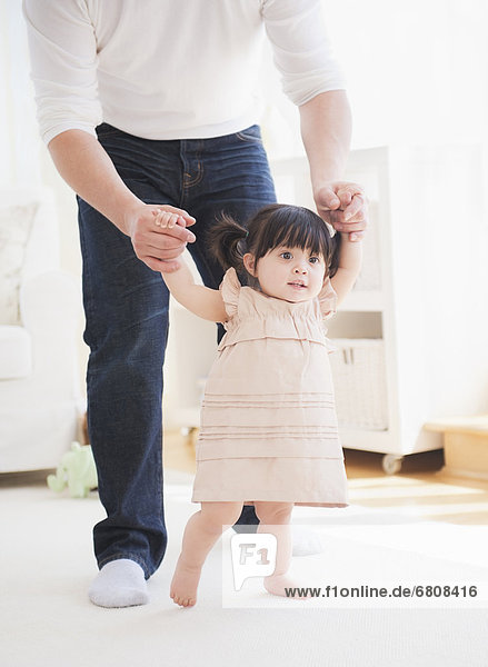 Father helping baby daughter (12-17 months) with her firsts steps