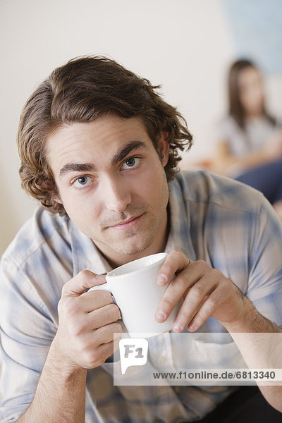 Portrait of young man holding mug  woman in background