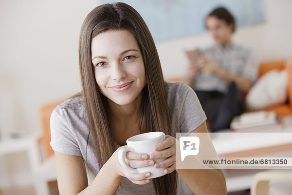 Portrait of young woman holding mug  man in background