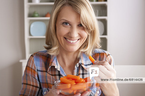 Portrait of mid adult woman with bowl of carrots