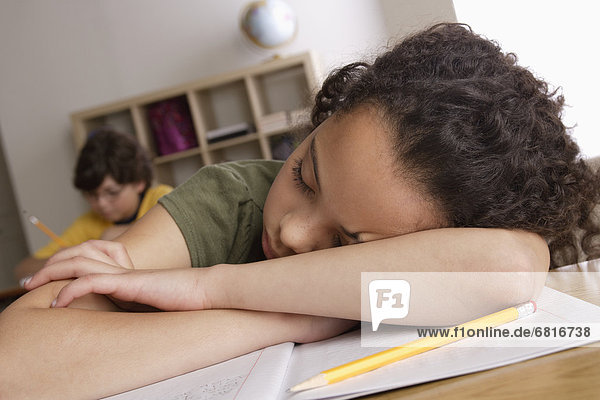 Girl (10-11) napping on desk with boy (10-11) in background