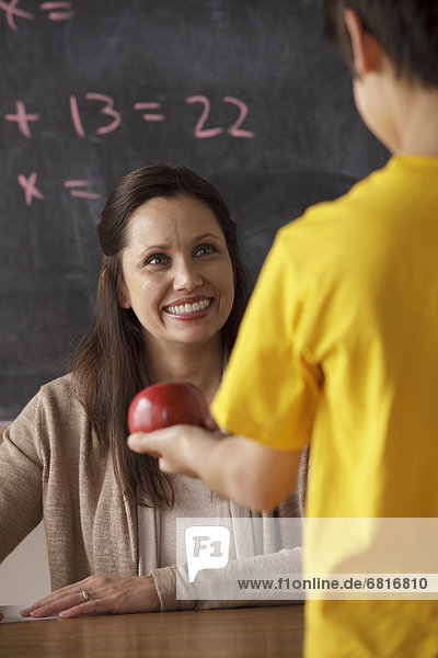 Schoolboy (12-13) giving apple to his teacher
