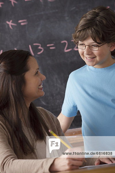 Schoolboy (10-11) and teacher face to face with blackboard in background