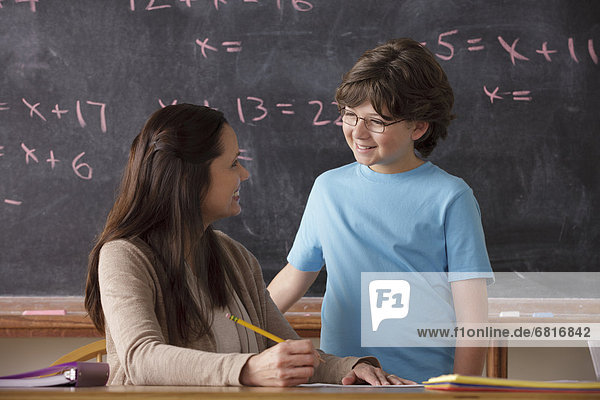 Schoolboy (10-11) and teacher face to face with blackboard in background