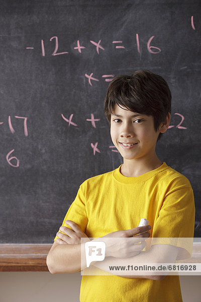 Portrait of schoolboy (12-13) standing in front of blackboard during math classes