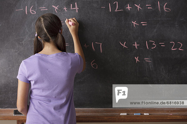 Portrait of schoolgirl (12-13) standing in front of blackboard during math classes