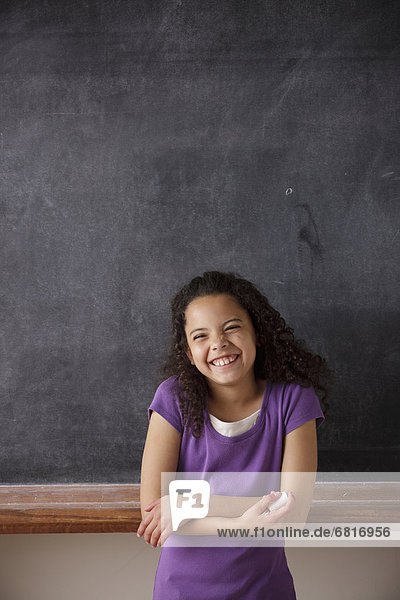 Portrait of schoolgirl (10-11) standing in front of blackboard