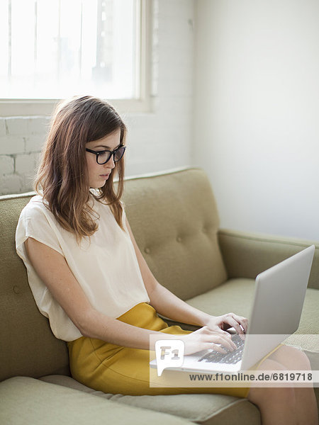 Young woman sitting on sofa with laptop