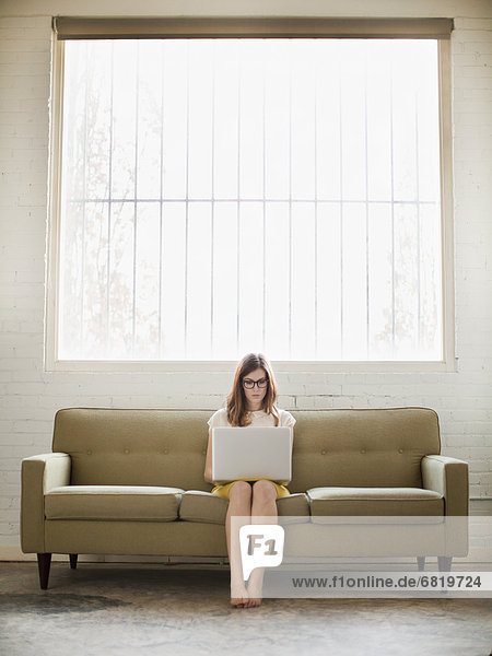 Young woman sitting on sofa with laptop