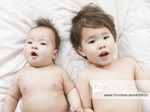 Mixed race siblings (2-5 months  2-3) lying in bed side by side