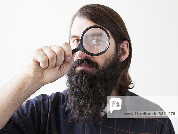 Bearded young man looking through magnifying glass
