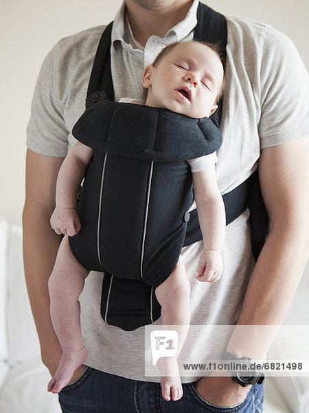 Young father holding baby daughter (2-3 months) in carrycot