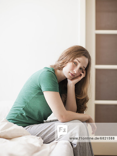 Sad young woman sitting in bed