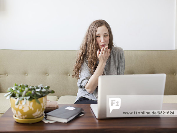Young woman blowing kiss while using laptop