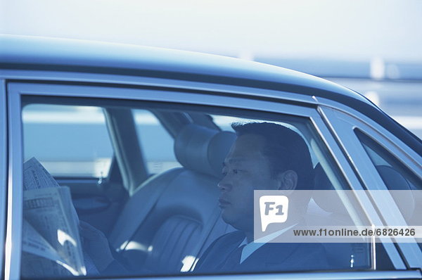 Mature businessman reading newspaper in car