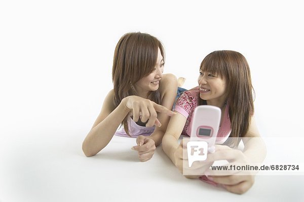 Zwei junge Frauen betrachten ein Mobiltelefon und lächelnd