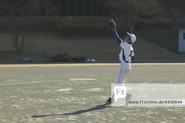 Boy in baseball uniform trying to catch a ball
